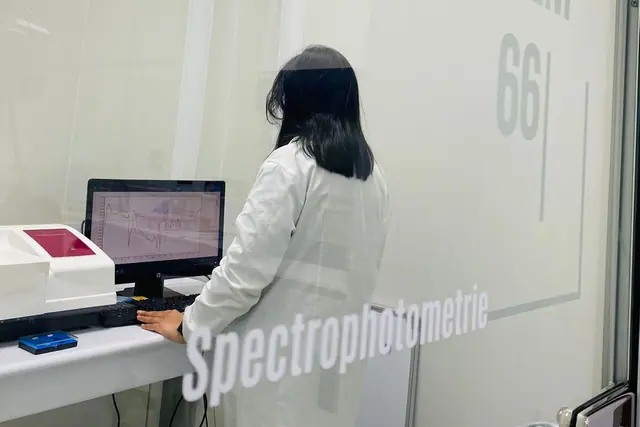 Technicienne au poste de spectrophotométrie du laboratoire System66, derrière une paroi vitrée.
